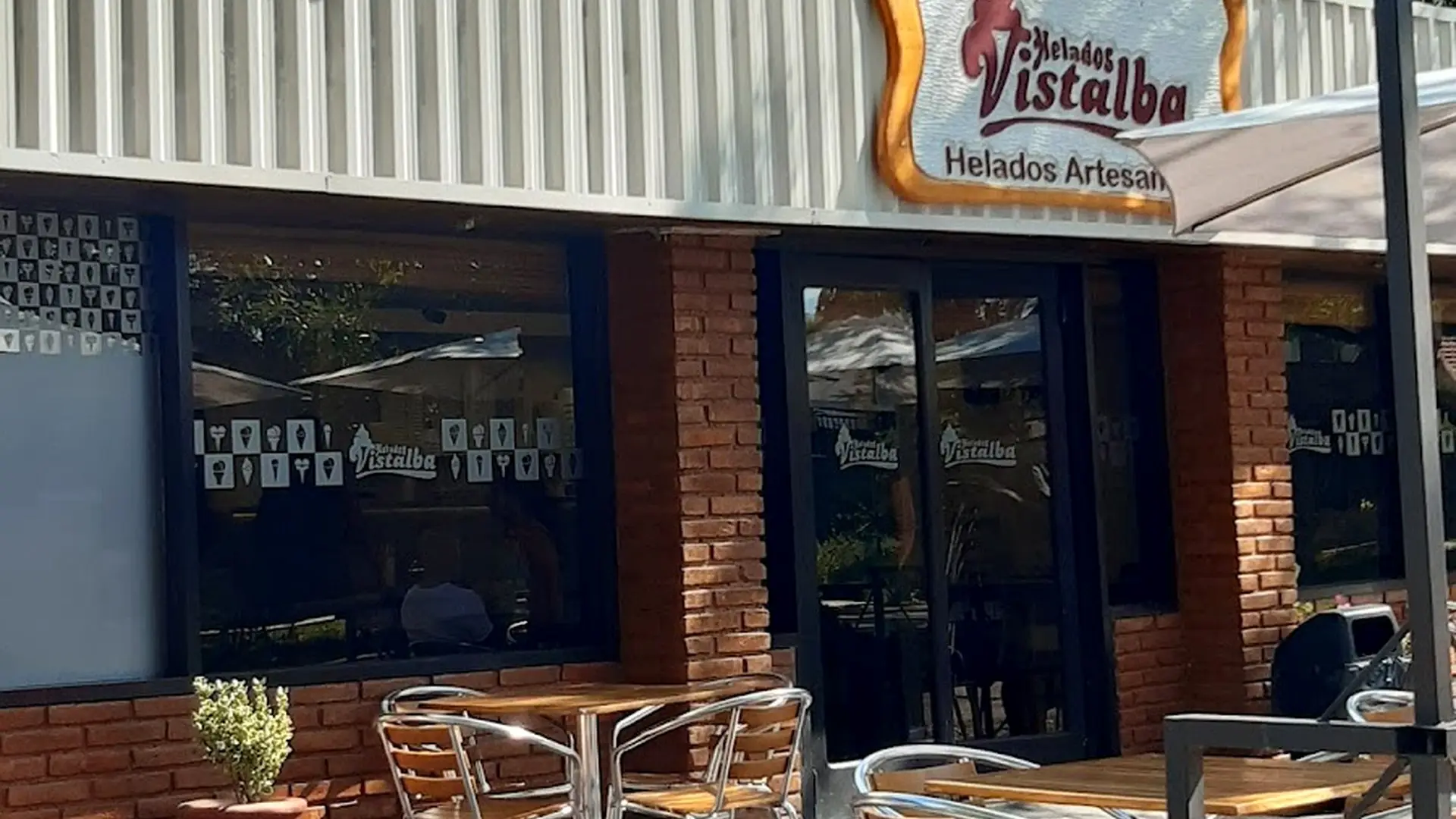 Frente del local de Helados Vistalba con cartel y mesas a la sombra