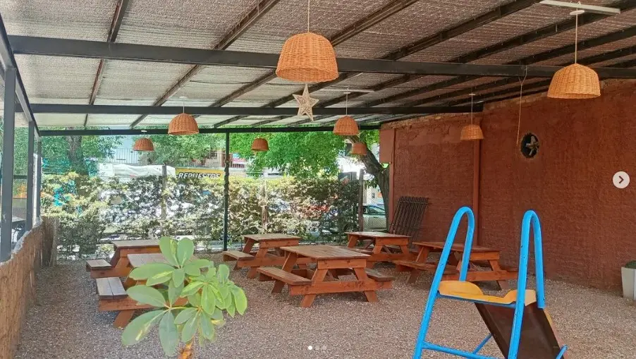 Terraza de Molino Pizza con mesas de madera bajo techo, rodeada de verde